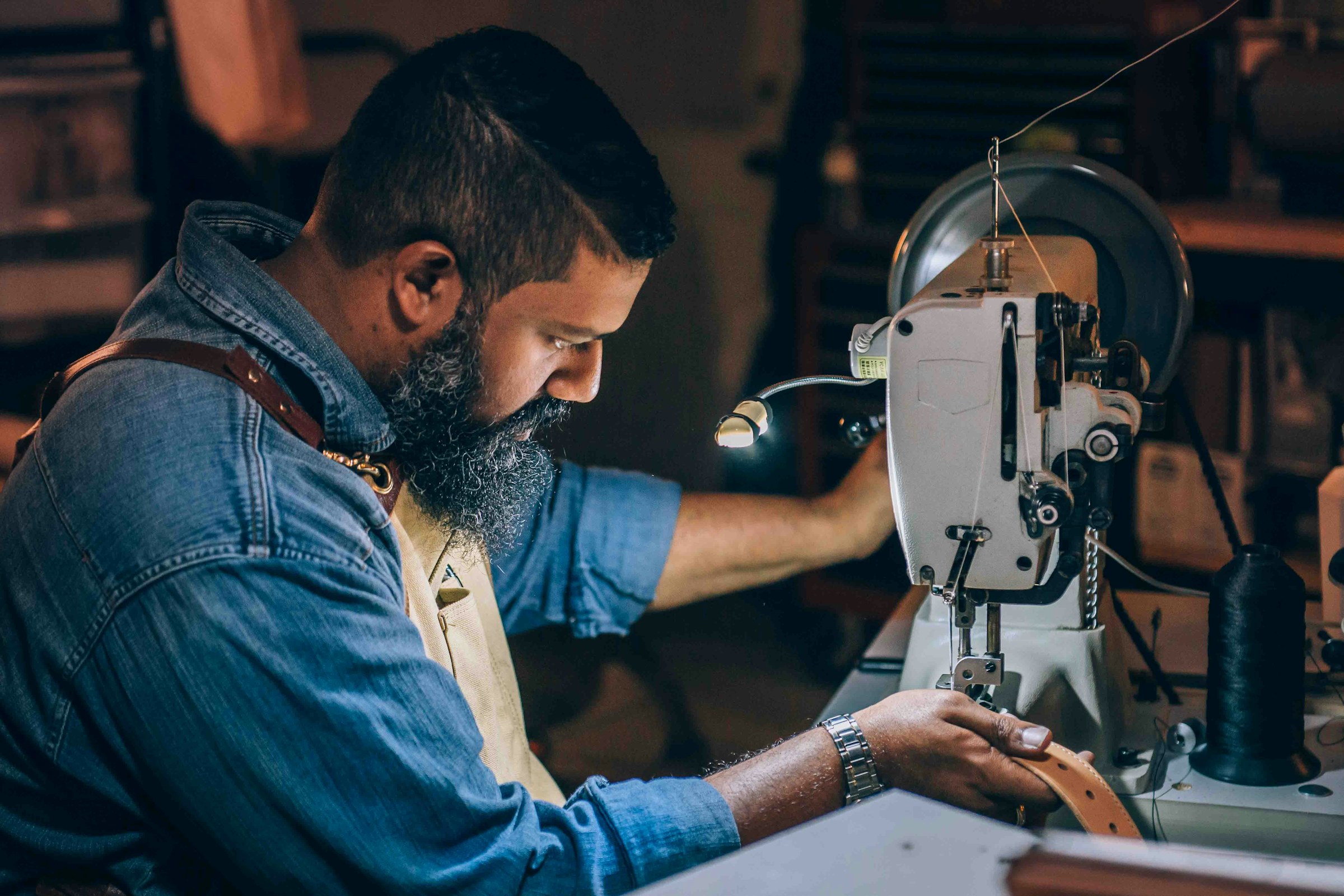 Garment craftsman at a sewing machine in a warm-lit atelier — manufacturing trust and craftsmanship